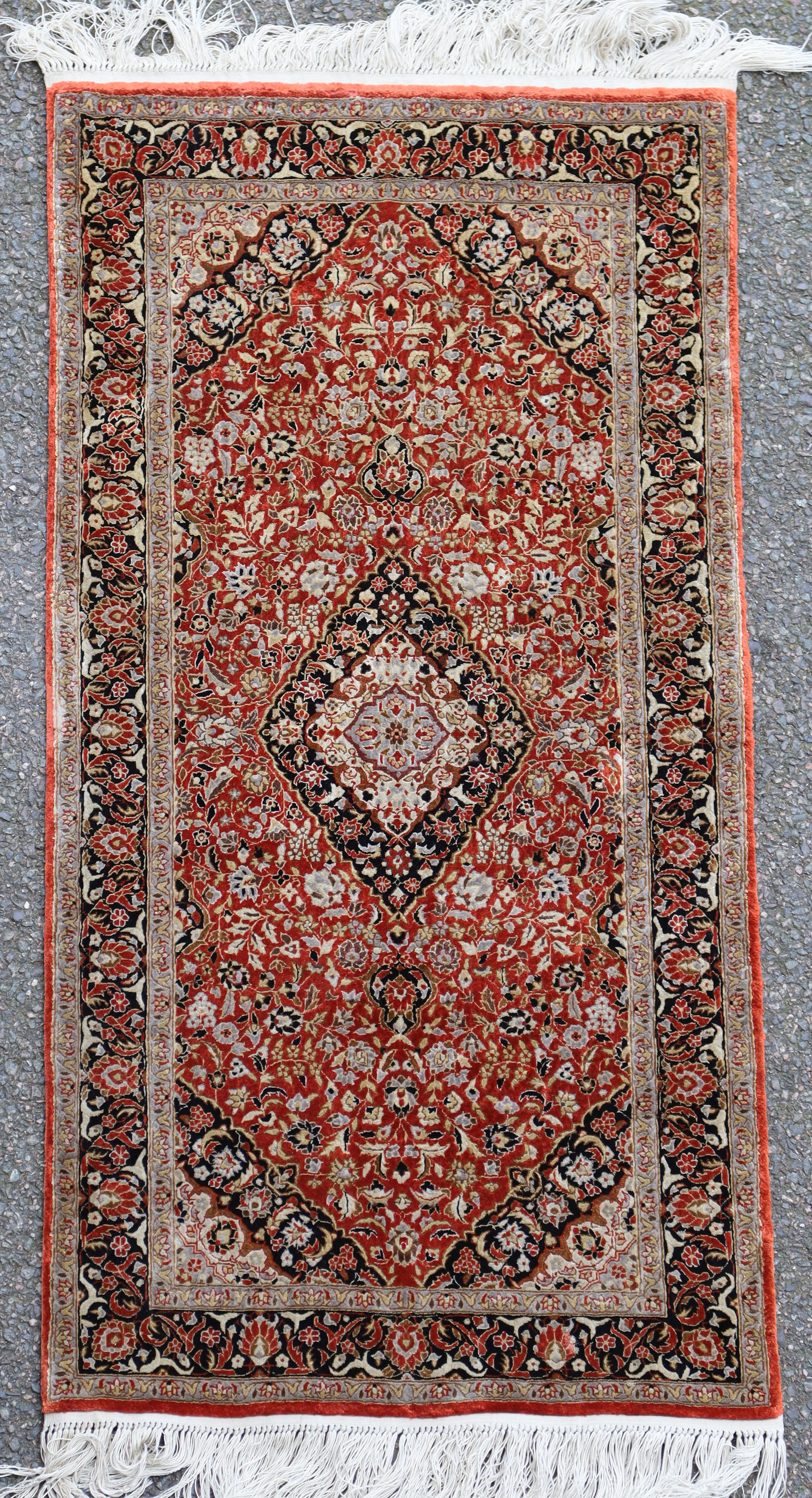 A Persian silk russet ground rug, with central medallion in a field of scrolling foliage and three