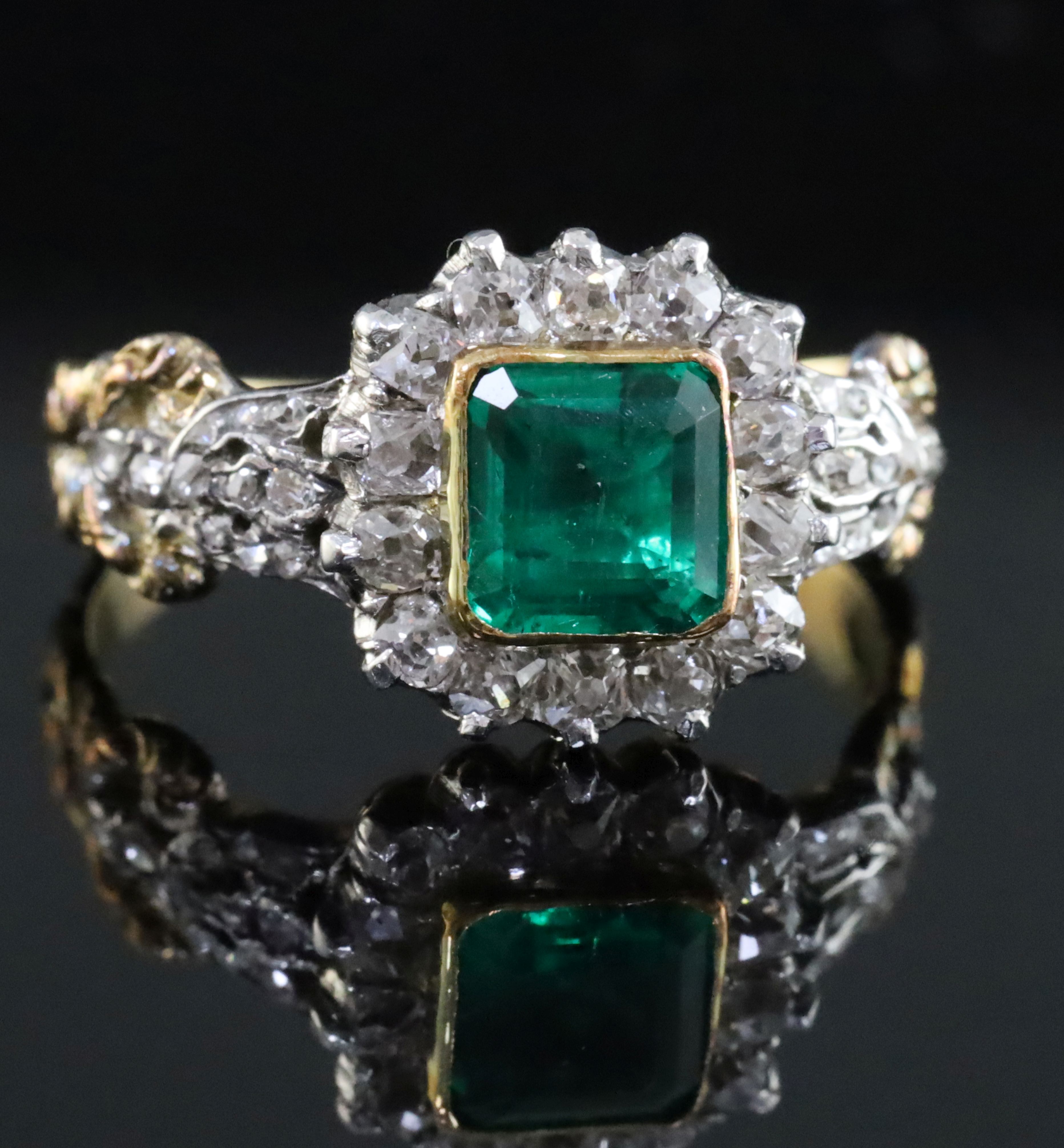 An antique 18ct gold, emerald and diamond cluster ring, the central square cut emerald (0.88ct)
