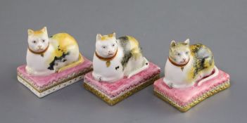 Three Derby porcelain figures of recumbent cats, c.1810-25, each with tortoiseshell markings, on a