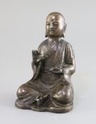 A Chinese bronze figure of a seated Luohan, 17th/18th century, holding a mongoose in his left