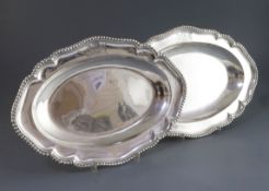 A near pair of George II/George III silver shaped oval meat dishes, with gadrooned borders and