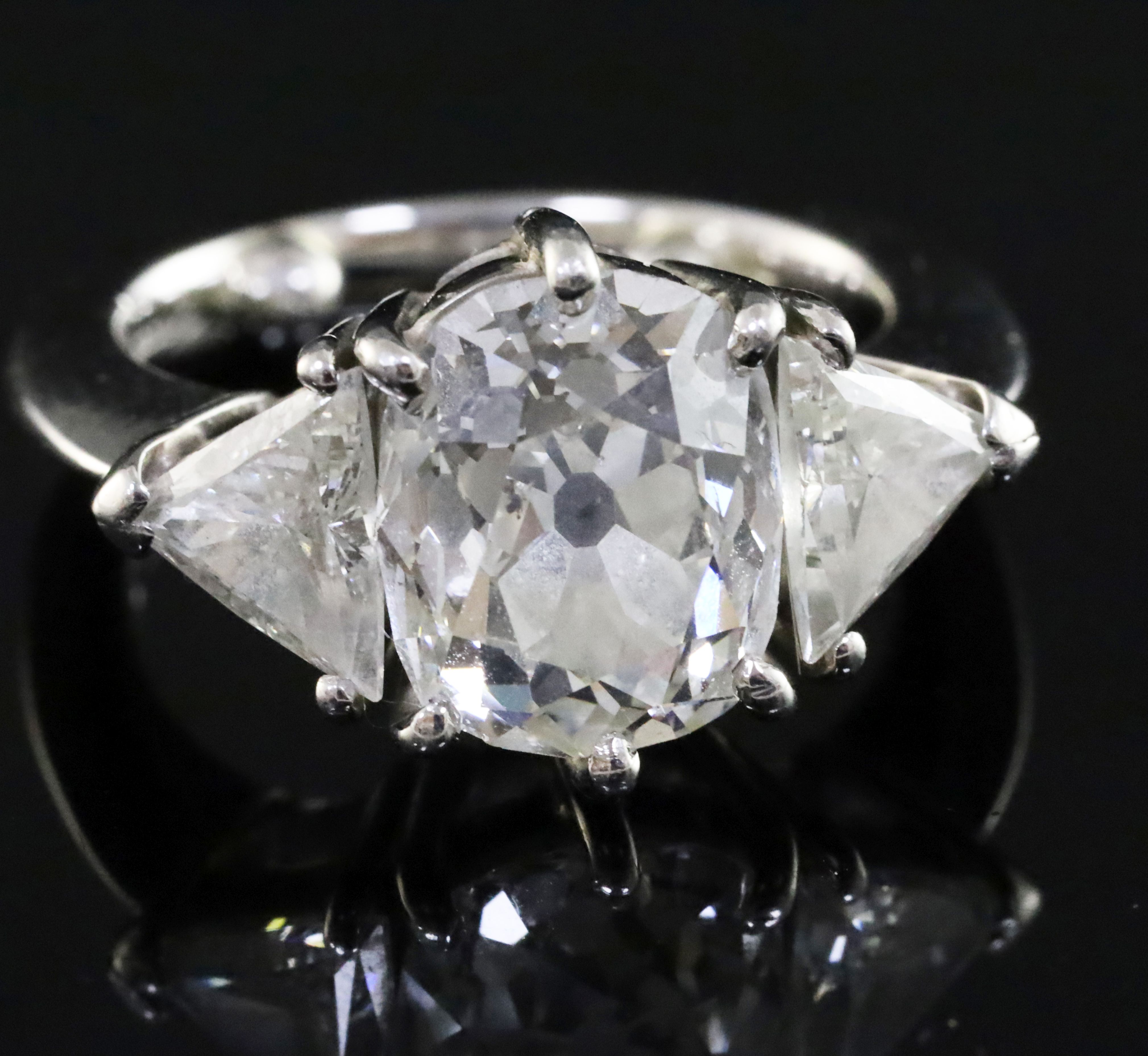 A modern platinum, oval cushion and trillion cut diamond set three stone ring, the central stone