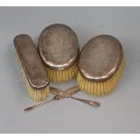 Three silver backed hair brushes and two butter knives, one silver.