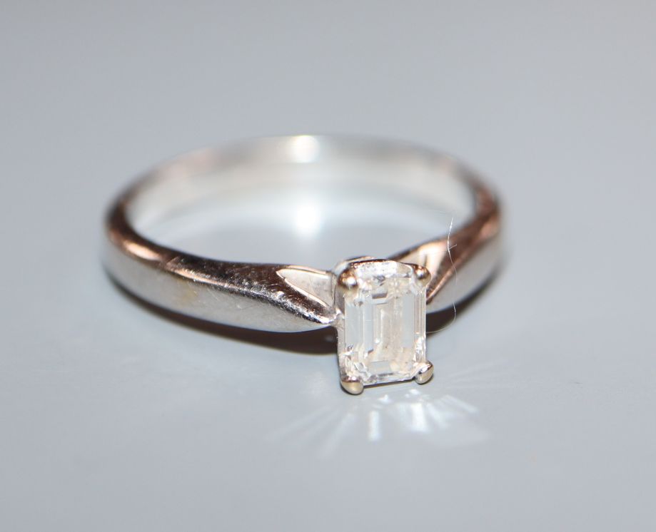 A modern 750 white metal and solitaire emerald cut diamond ring, size J/K