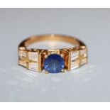 A modern 750 yellow metal, single stone sapphire dress ring, flanked with round and trapeze cut