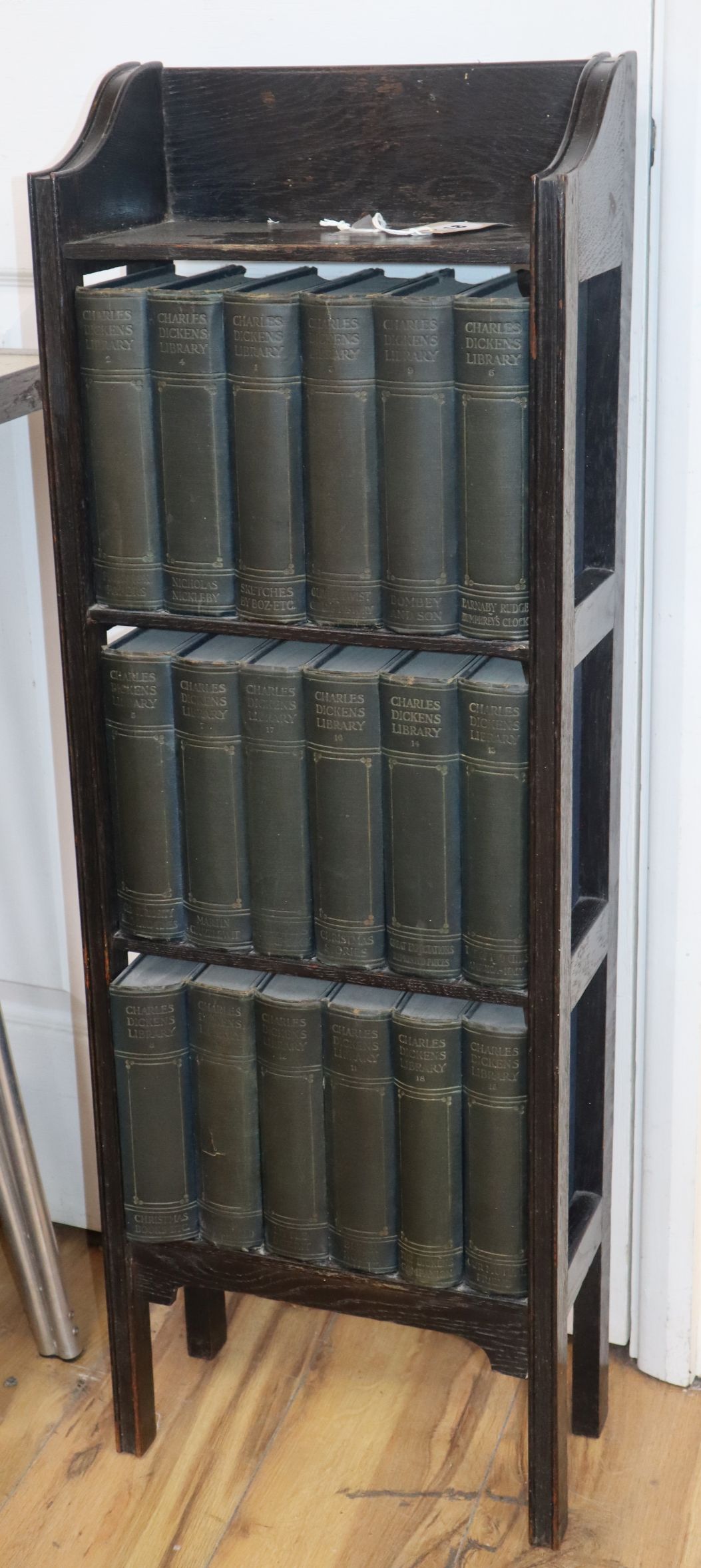 A narrow open fronted bookcase and works of Charles Dickens