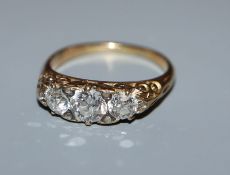 A diamond three-stone ring, claw-set in yellow metal with scrolled mount, size M.