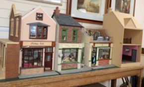 A group of three dolls house models of shops with figures and accessories and an unfinished doll's