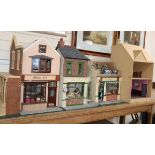 A group of three dolls house models of shops with figures and accessories and an unfinished doll's