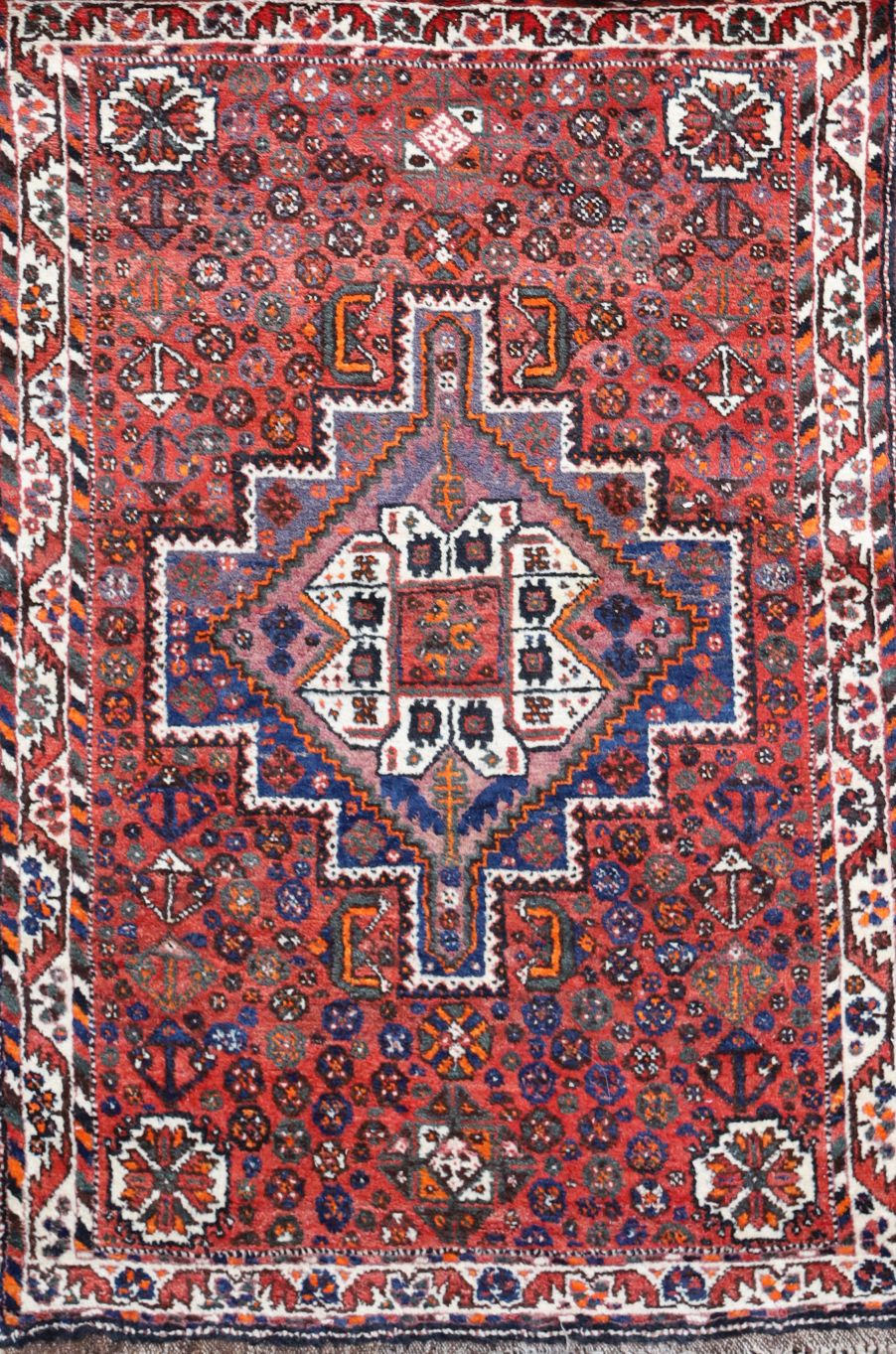 A Shiraz design red ground rug, with central polygon in a field of flower heads and three row