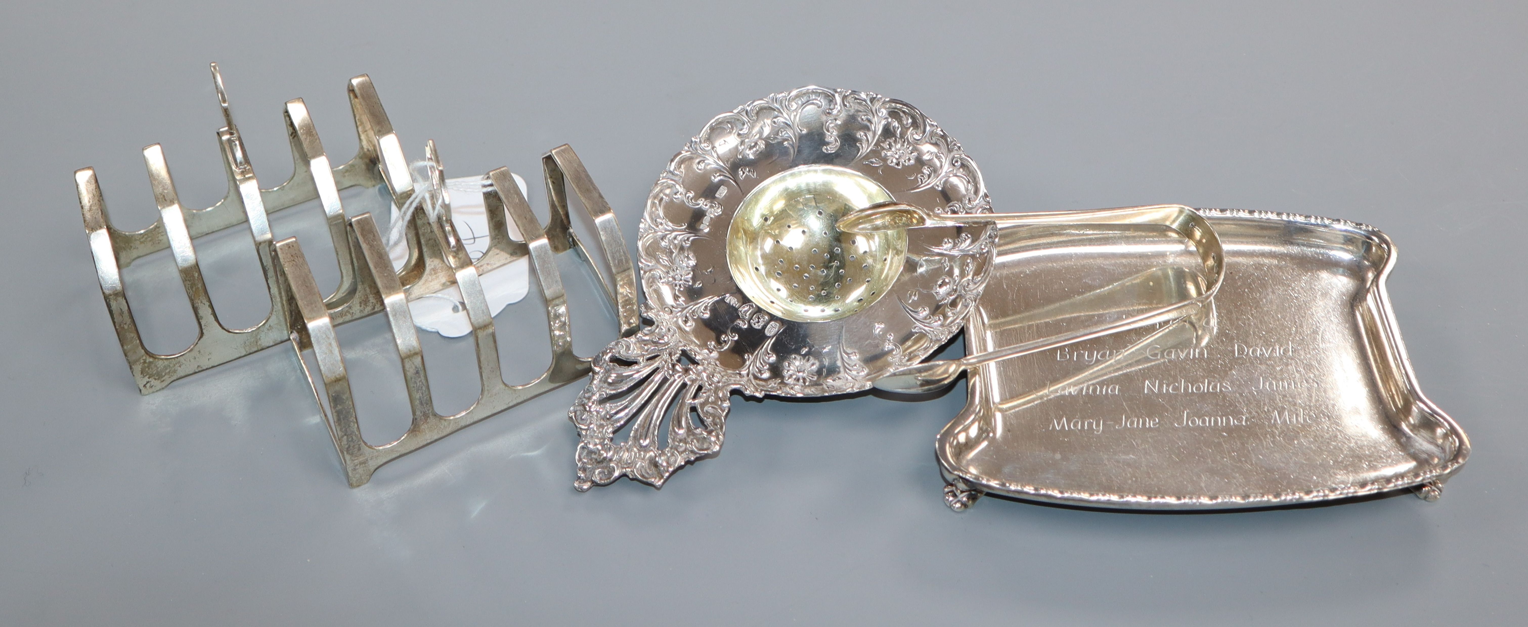 A pair of silver toastracks, a silver presentation dish, a pair of silver sugar tongs and a white