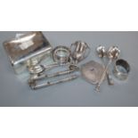 A silver cigarette box, silver pencil, two silver napkin rings, small silver trophy cup, five silver