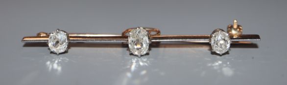 An early 20th century yellow metal and three stone oval cushion cut diamond set bar brooch, 52mm.