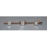 An early 20th century yellow metal and three stone oval cushion cut diamond set bar brooch, 52mm.