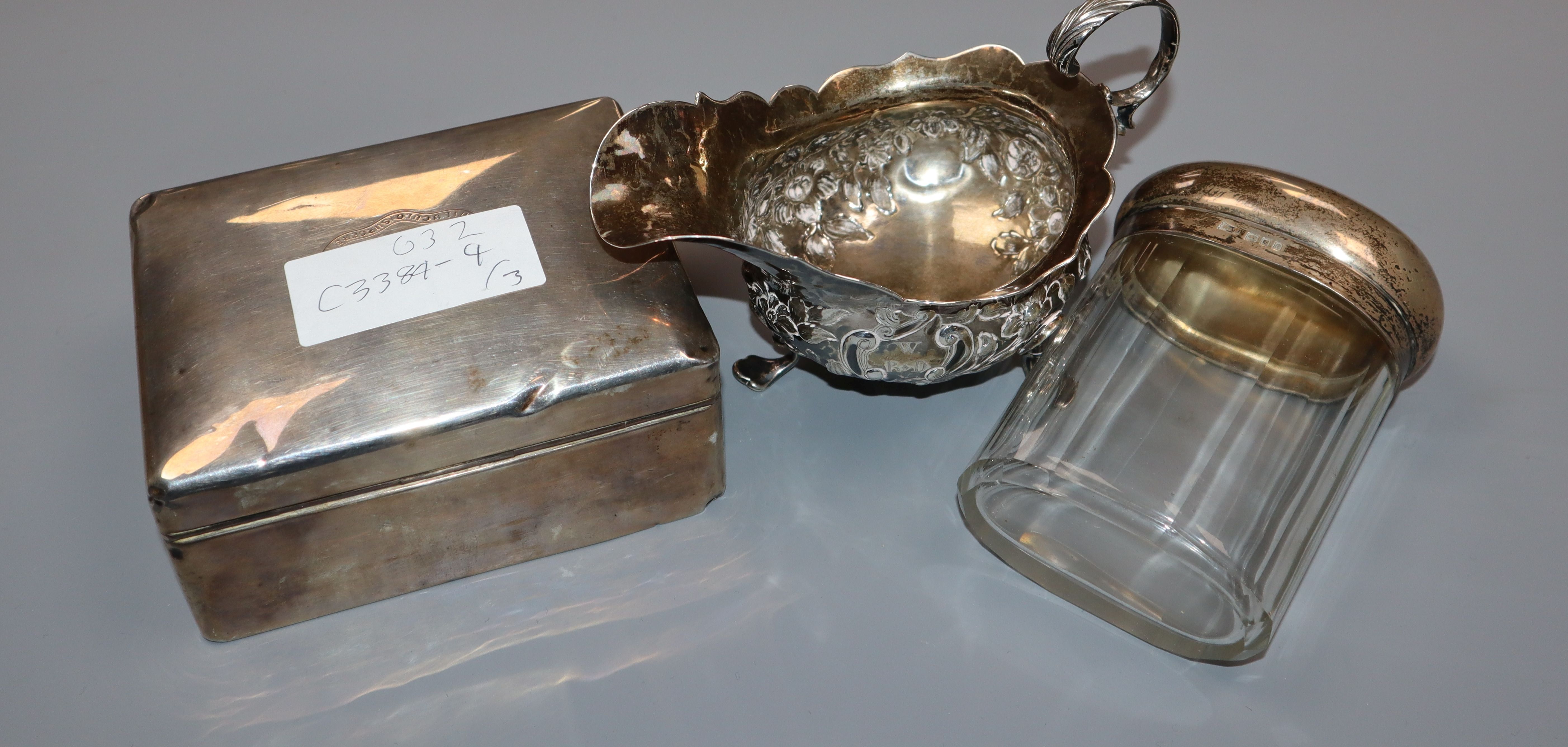 A George III silver sauce boat, a silver cigarette box and silver mounted glass toilet bottle.