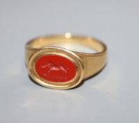 An antique yellow metal and carnelian signet ring, the oval stone carved with the figure of a