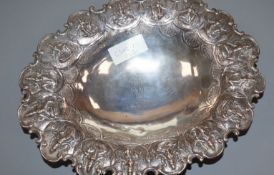 An early 20th century Indian white metal oval bowl, the border embossed with deities, 31cm, 14 oz.