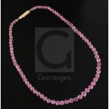 A gold and graduated round cut ruby line necklace, set with seventy four stones, 40cm