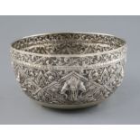 An early 20th century Thai silver bowl, embossed with deities amid scrolling foliage, on three