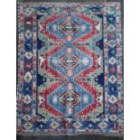 A Caucasian Kazak red and blue ground rug, with three central medallions in a field of hooked motifs