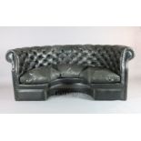 A buttoned black leather concave settee, with triple squab cushions and brass studding, W.7ft D.
