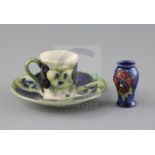 A Moorcroft 'pansy' pattern coffee cup and saucer, c.1915 and a similar later miniature vase, the