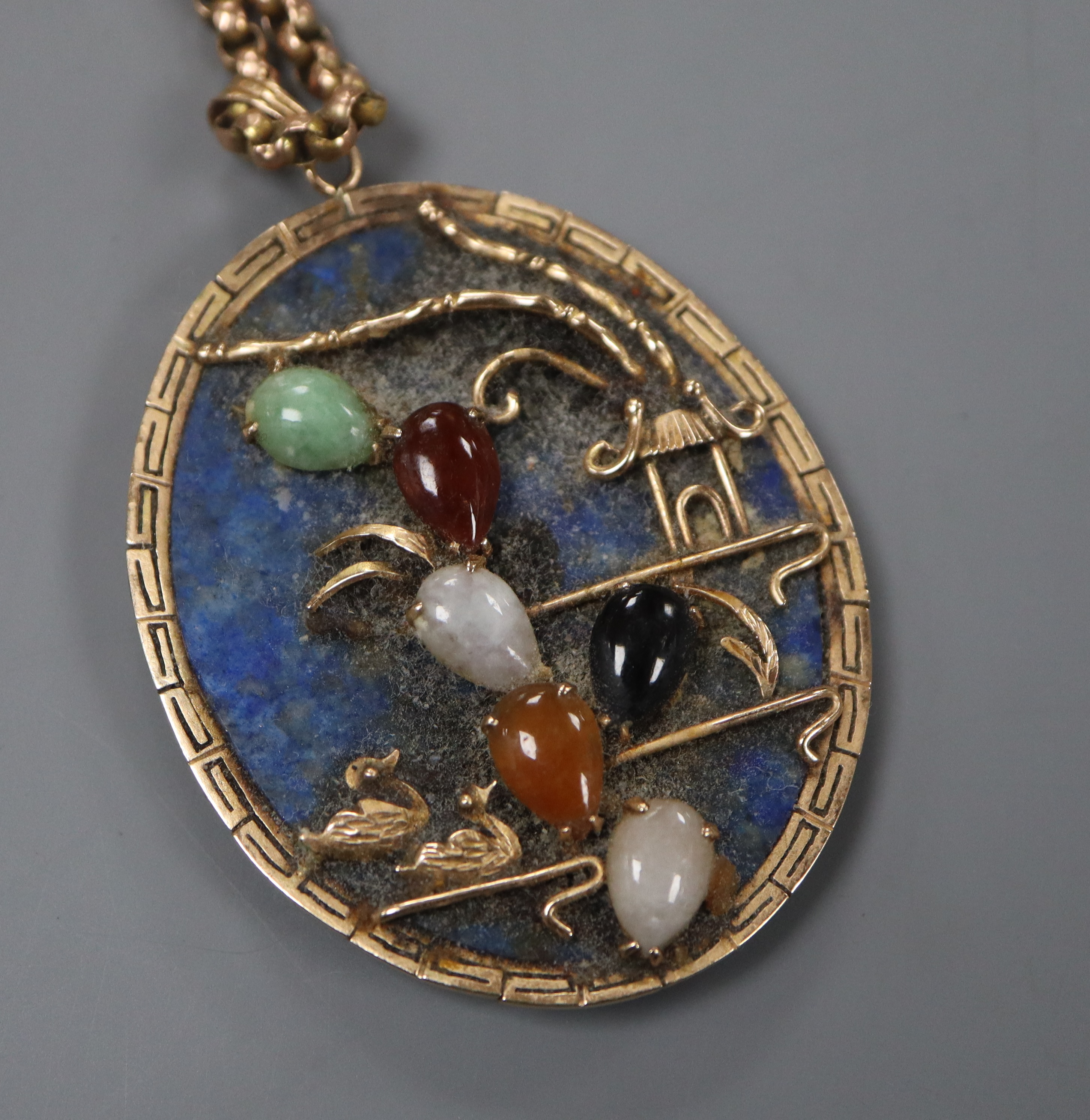 A yellow metal and multi gem set mounted lapis lazuli set oval pendant, on an early 20th century