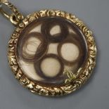 An early 19th century yellow metal mounted circular mourning pendant, with hair beneath glazed