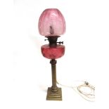 A VICTORIAN OIL LAMP with cranberry glass reservoir and brass reeded column base, 69cm high overall