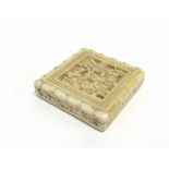 A CHINESE CARVED IVORY BOX 6cm square, the sliding lid opening to reveal seven piece geometric