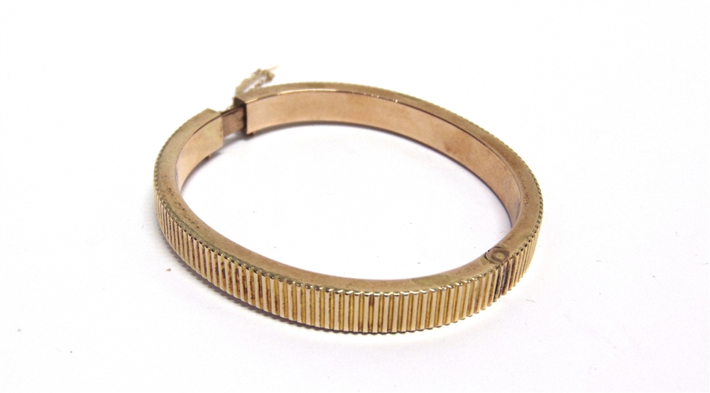 AN EARLY 20TH CENTURY ROSE GOLD HOLLOW HINGED BANGLE of hollow reeded-rectangular section, on a