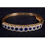 AN EDWARDIAN GOLD, SAPPHIRE AND DIAMOND HINGED BANGLE the front designed as a row of eleven