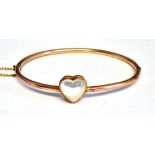 AN EARLY 20TH CENTURY GOLD AND MOONSTONE HINGED BANGLE the front with an 11mm high heart-shaped