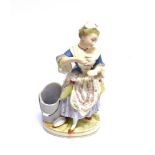 A CONTINENTAL FIGURE OF A LADY standing beside a grain bucket, holding a cup and saucer, 21.5cm