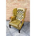 A GREEN LEATHER BUTTON UPHOLSTERED WING ARMCHAIR on square moulded supports