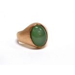 AN ORIENTAL YELLOW METAL AND OVAL CABOCHON PALE-GREEN JADEITE SINGLE STONE RING on a satinised