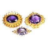 THREE VICTORIAN GOLD AND AMETHYST BROOCHES Comprising; an oval mixed-cut amethyst rub-over set