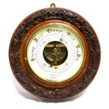 AN EDWARDIAN ANEROID BAROMETER with visible mechanism, the walnut case with carved decoration,