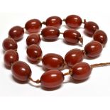 AN EARLY 20TH CENTURY IMITATION-RED-AMBER BEAD NECKLACE the oval beads approx. 18mm long and knotted
