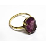 AN OVAL AMETHYST-COLOURED PASTE SINGLE STONE RING the mixed-cut stone claw set in white between