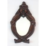 A CONTINENTAL WOODEN FIGURAL MIRROR modelled as a crossed legged figure holding his head in his
