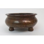 A CHINESE BRASS CENSER the everted rim above a short bulbous body and on three feet, cast six