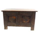 AN OAK COFFER the hinged two plank top enclosing a candle box and above a panelled front carved with