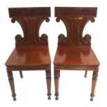 A PAIR OF MID 19TH CENTURY MAHOGANY HALL CHAIRS with scroll shaped backs above a solid seat and on