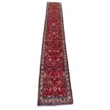 A RED GROUND HAMADAN RUNNER with allover floral design and cream border, 530cm x 80cm Condition