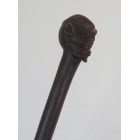 AN AFRICAN HARWOOD STICK the handle carved with a head and above a male figure running and holding a