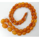 A STRING OF AMBER COLOURED BEADS largest bead 22mm x 17mm, smallest 11mm x 7.5mm, overall length