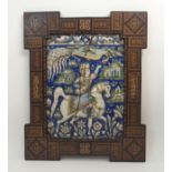 A PERSIAN POLYCHROME MOULDED POTTERY TILE decorated with a prince on horseback feeding a bird and