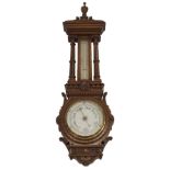 A VICTORIAN CARVED OAK ANEROID WHEEL BAROMETER/THERMOMETER with urn finial above fluted columns
