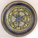 A LARGE TERRACOTTA CHARGER with geometric and banded decoration, in shades of green, blue and cream,